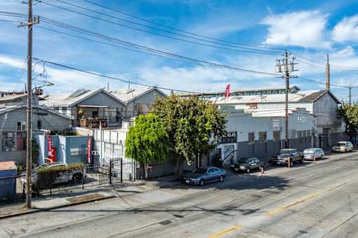 A street view with cars parked on the side of the road and a building with a red flag on top in the background.