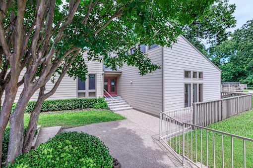 A house with a grey exterior and a red door is surrounded by greenery.