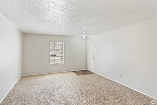 a spacious living room with carpet and a door to a bedroom