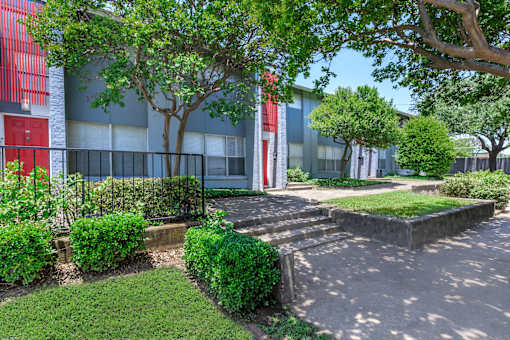 a sidewalk in front of a building with trees and bushes