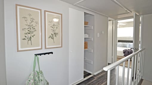 A hallway with a white railing and two framed pictures on the wall.