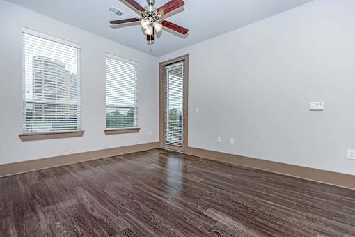an empty living room with a ceiling fan and windows
