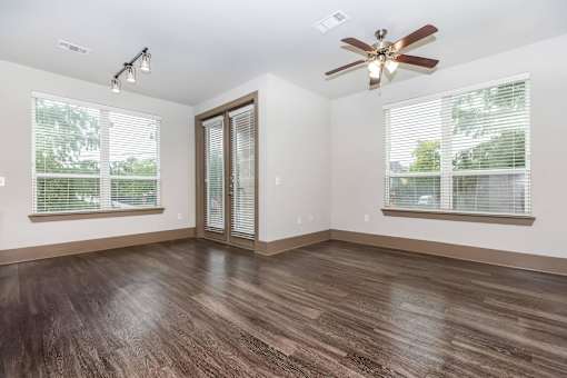 an empty living room with a ceiling fan and two windows