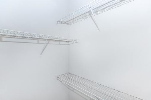 a walk in closet with white walls and shelves and a mirrored closet door