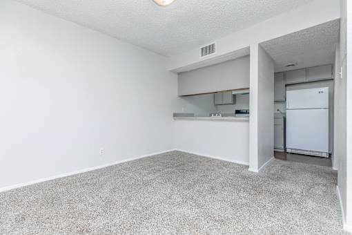 A white room with a carpeted floor and a white refrigerator in the corner.