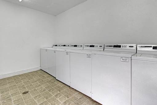 a row of washes and dryers in an empty laundry room