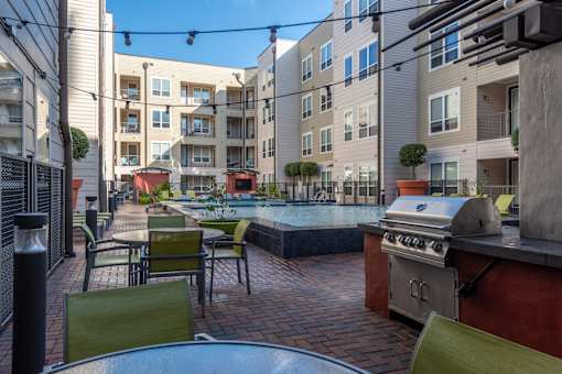 a patio with tables and chairs and a pool in front of an apartment building