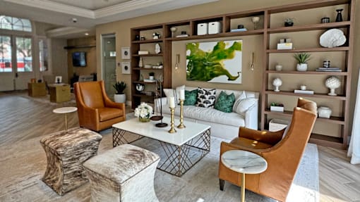 A living room with a white couch, brown chairs, and a large painting on the wall.