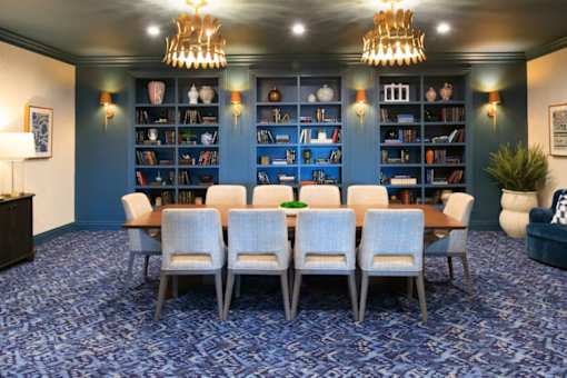 A room with a long table and chairs with a bookshelf in the background.