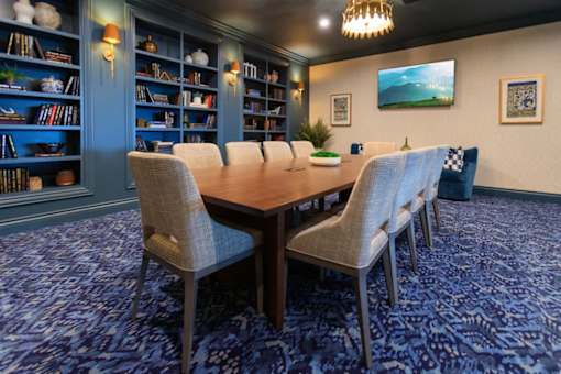 A room with a large table surrounded by chairs and bookshelves filled with books.