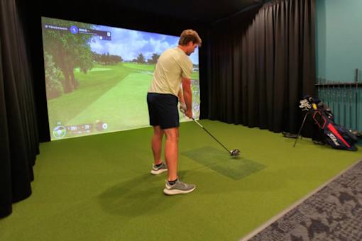 A man is playing golf in a room with a screen showing a golf course.