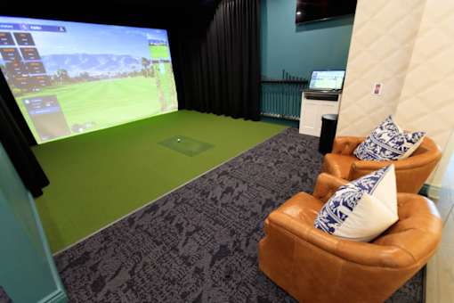 A room with a large screen and a brown chair with a blue and white pillow.