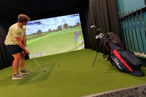 A man is playing golf in a room with a large screen showing a golf course.