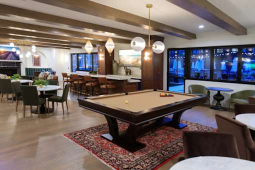 A pool table is in the middle of a room with a bar and a fireplace.