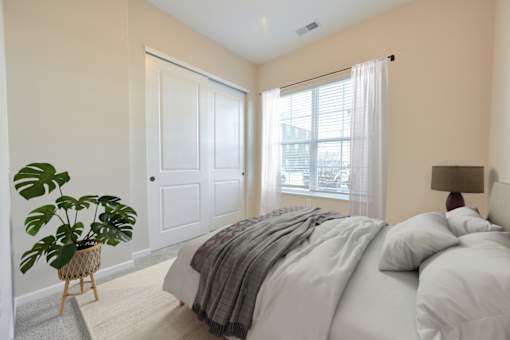 A bedroom with a bed, a potted plant, and a window.
