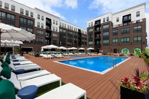 A large outdoor pool area with sun loungers and umbrellas in front of a multi-story building.