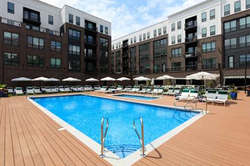 A large swimming pool surrounded by wooden deck chairs and umbrellas.