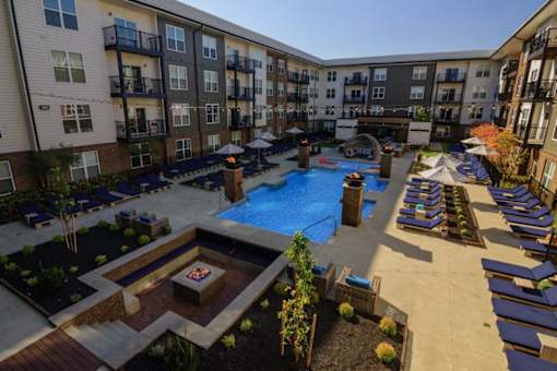 A large outdoor pool area with lounge chairs and a fire pit surrounded by apartment buildings.