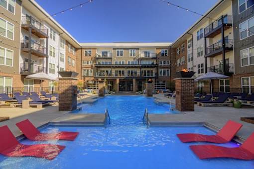 A swimming pool surrounded by red lounge chairs in front of apartment buildings.