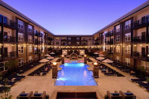 A swimming pool surrounded by lounge chairs and balconies with lights strung up.