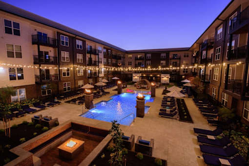 A pool surrounded by lounge chairs and lit string lights.