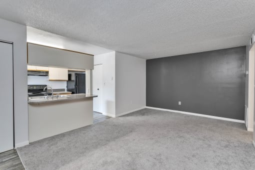 the living room and kitchen of an apartment with a gray carpet and white walls at Windover Oaks Apartments, Titusville, FL