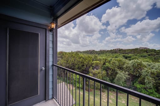 a balcony with a door and a view of trees and a cloudy sky
