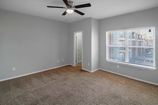 A room with a ceiling fan and a window overlooking a cityscape.