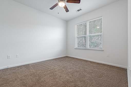 A room with a ceiling fan and a window with a view of trees.