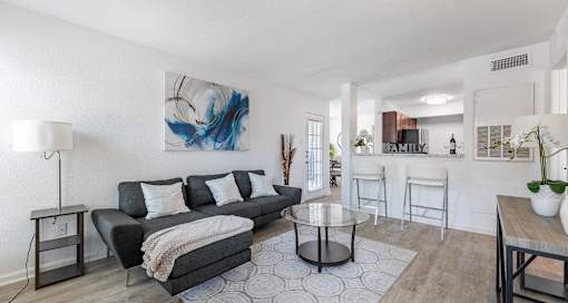 A modern living room with a black couch and a large abstract painting on the wall.