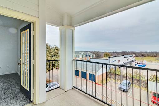 A balcony with a view of a parking lot and buildings.