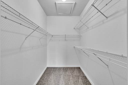 A white walk in closet with a carpeted floor.