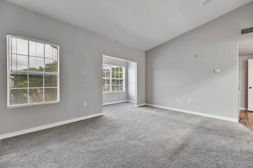 A spacious room with grey carpeting and two windows at Waters at Elm Creek, Texas