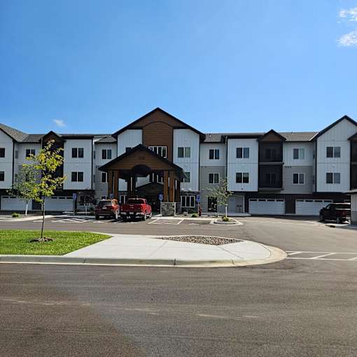 A large white building with a brown roof and a parking lot in front.