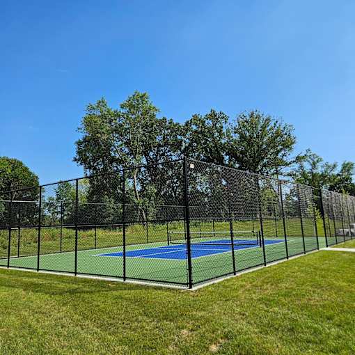 A tennis court enclosed by a black fence with trees in the background.