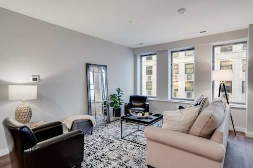 A living room with a black chair, a beige couch, and a black and white rug.