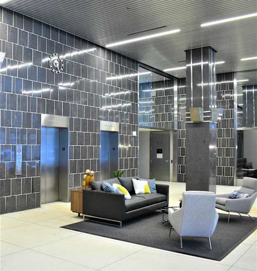 A modern living room with a grey couch, a grey chair and a black and white tiled wall.