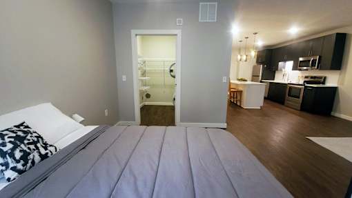 A bedroom with a bed in the foreground and a kitchen in the background.