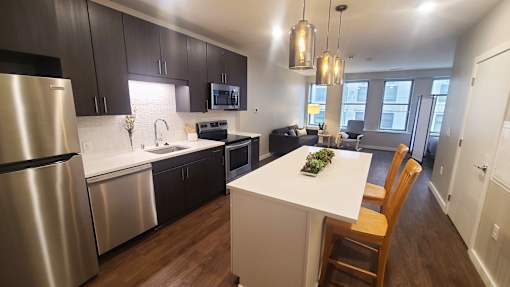 A modern kitchen with a white island and wooden chairs.