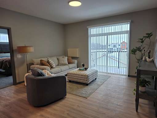A living room with a grey couch, a white ottoman, and a wooden floor.