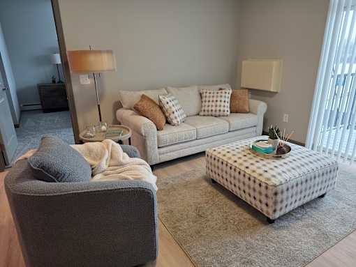 A grey chair with a pillow and a grey couch with pillows and blankets in a living room.