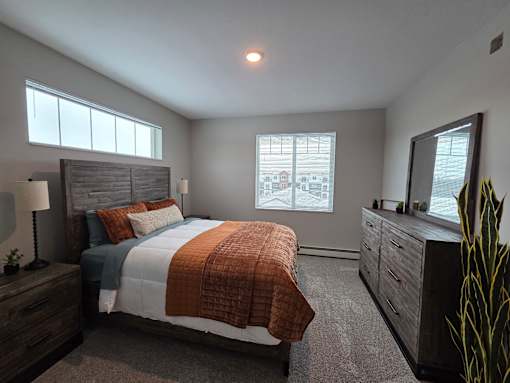 A bedroom with a large bed, a nightstand with a lamp, and a dresser with a mirror.