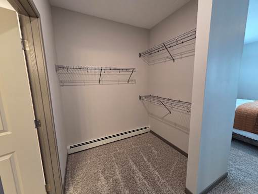 A walk-in closet with white walls and grey carpeting.