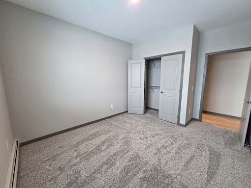A room with grey carpet and a grey wall with a white door and a grey wardrobe.