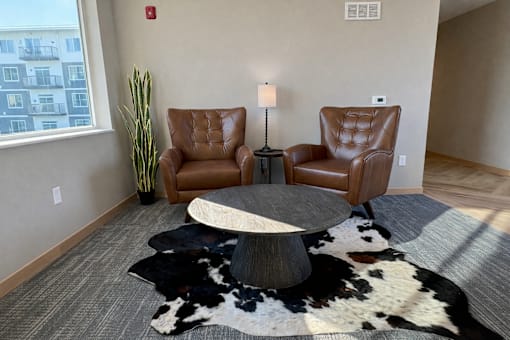A living room with two leather chairs, a table, and a cowhide rug.