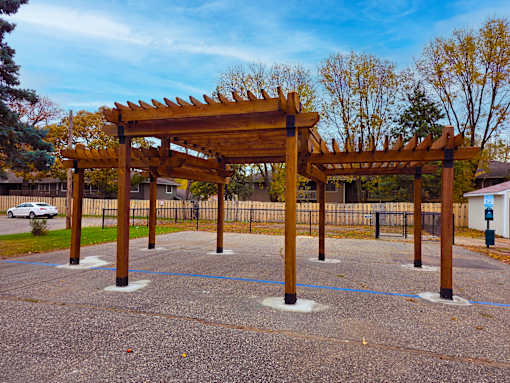 A wooden pergola structure in the middle of a paved area.