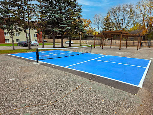 A blue tennis court surrounded by trees and a fence.
