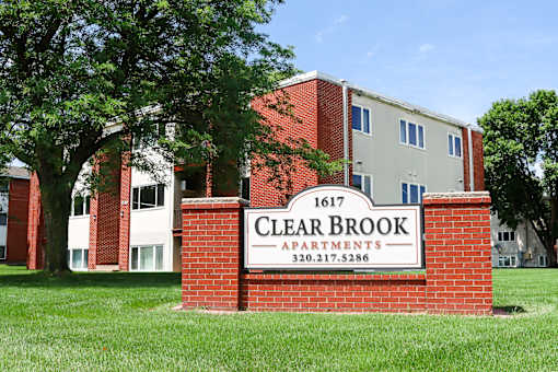 A sign for Clear Brook Apartments is in front of a brick building.