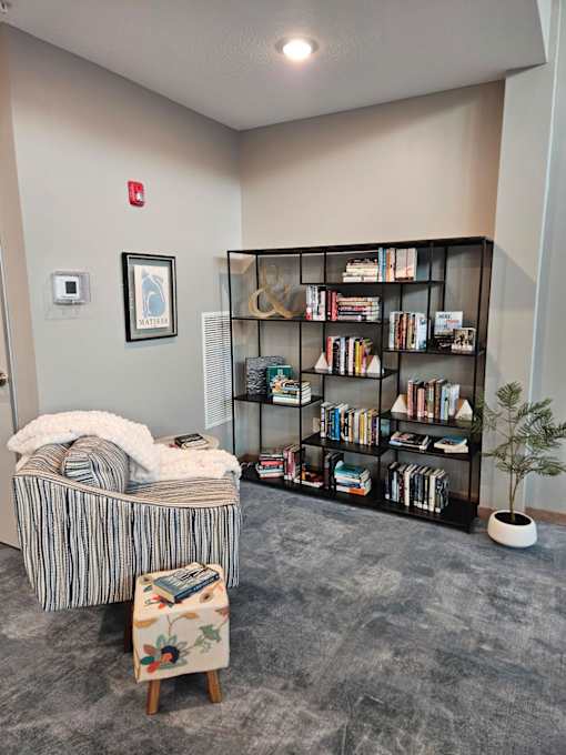 A room with a bookshelf, a chair, and a small tree.