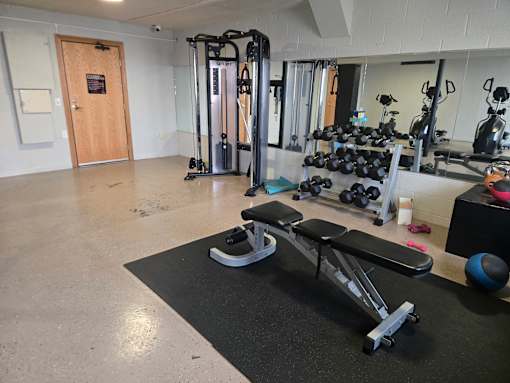 A gym with a variety of equipment including a treadmill, weights, and a bench.